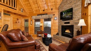A cozy cabin interior with leather sofas, a stone fireplace, and a television mounted on the wall. - Sunset Views • Hot Tub • Pool Table • Sleeps 5 (Sevierville)