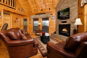 A cozy cabin interior with leather sofas, a stone fireplace, and a television mounted on the wall. - Sunset Views • Hot Tub • Pool Table • Sleeps 5 (Sevierville)