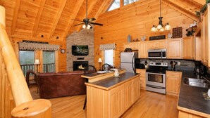 A wooden cabin interior with a kitchen, dining area, and a fireplace. - Sunset Views • Hot Tub • Pool Table • Sleeps 5 (Sevierville)