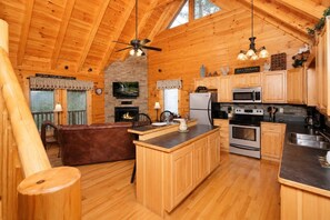 A wooden cabin interior with a kitchen, dining area, and a fireplace. - Sunset Views • Hot Tub • Pool Table • Sleeps 5 (Sevierville)
