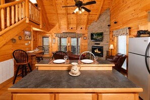 A wooden cabin interior with a dining area, fireplace, and a kitchen with a refrigerator. - Sunset Views • Hot Tub • Pool Table • Sleeps 5 (Sevierville)