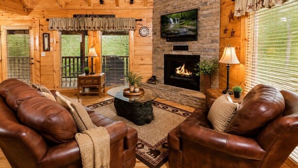 A log cabin interior with a stone fireplace, leather sofas, a television, and a wooden ceiling. - Sunset Views • Hot Tub • Pool Table • Sleeps 5 (Sevierville)
