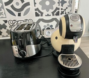 A toaster and a coffee maker on a table with a patterned wall in the background. - Waterfront apartment| Towels and sheets (Saint-Gilles-Croix-de-Vie)
