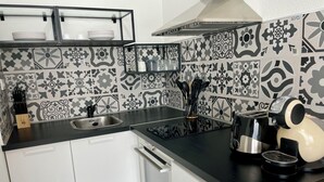 A kitchen with a black countertop, white cabinets, a stainless steel sink, a coffee maker, and patterned backsplash tiles. - Waterfront apartment| Towels and sheets (Saint-Gilles-Croix-de-Vie)