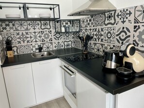 A kitchen with a black countertop, white cabinets, a stainless steel sink, a coffee maker, and patterned backsplash tiles. - Waterfront apartment| Towels and sheets (Saint-Gilles-Croix-de-Vie)
