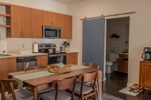 A compact kitchen with wooden cabinets, a microwave, a stove, and a dining area with a table and chairs. - Sipped Away: King Beds, Walk in Closets (Traverse City)
