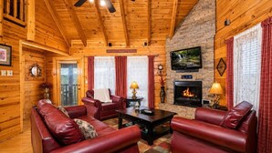 Ein Interieur einer Blockhütte mit Kamin, Ledersofas und einem an der Wand befestigten Fernseher.