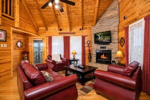 Ein Interieur einer Blockhütte mit Kamin, Ledersofas und einem an der Wand befestigten Fernseher.