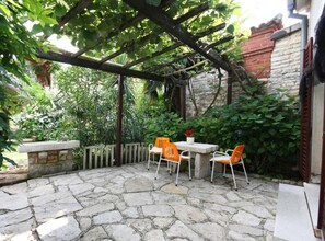 Une terrasse en pierre agrémentée d’une pergola, de coins salon extérieurs et d’une végétation luxuriante.