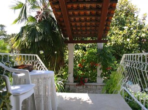 Ein überdachter Außenbereich zum Sitzen mit einer Pergola, weißen Stühlen und Blumentöpfen.