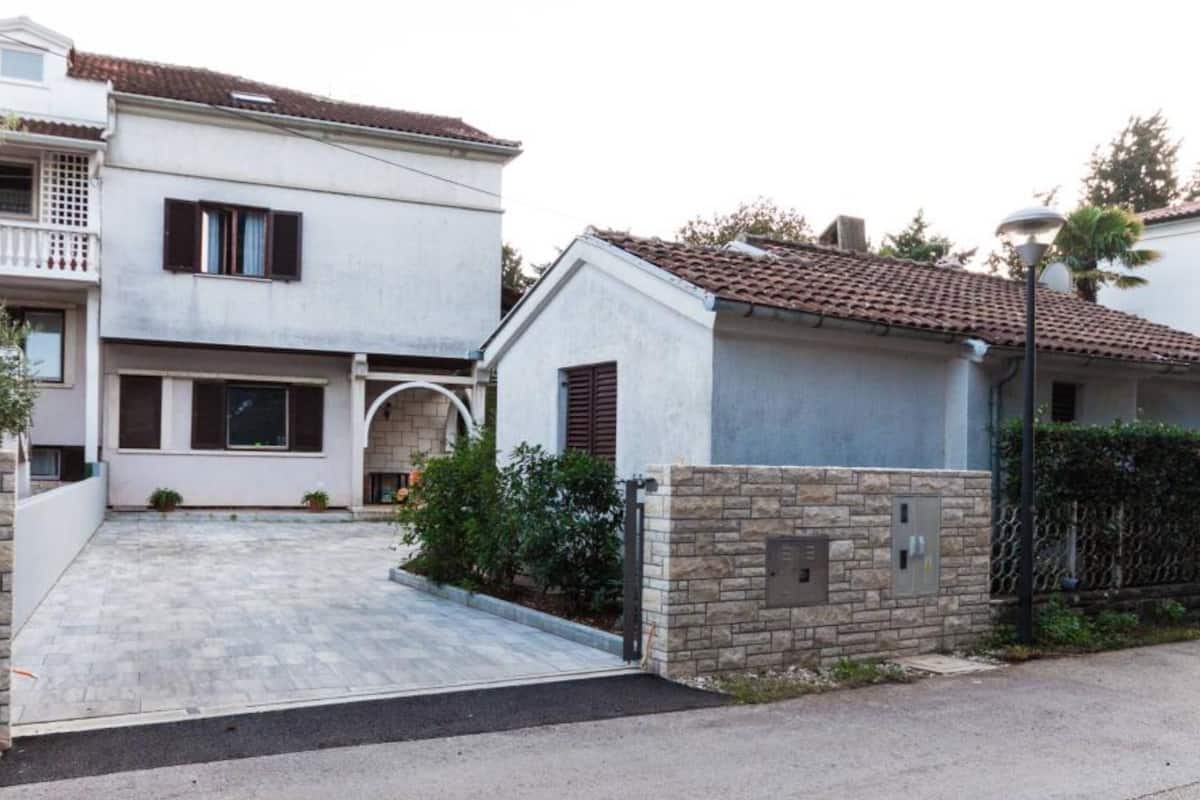 Un immeuble résidentiel avec une allée pavée, un mur en pierre et un petit porche d’entrée.