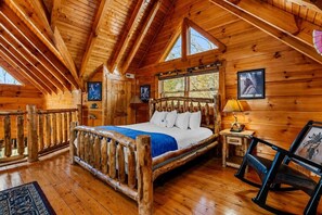 Eine Holzhütte mit einem Bett, einem Nachttisch, einem Stuhl und einem Fenster.