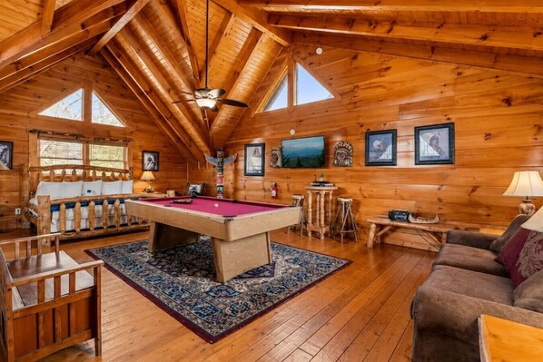 A wooden cabin interior with a pool table, a sofa, a television, and framed pictures on the walls. - Cozy Cabin w View, Hot Tub, Pool Table & Fireplace (Sevierville)
