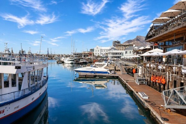 A marina with boats docked, a wooden pier, and buildings with outdoor seating. - Table Mountain Signature Suite  City Views (Cape Town)