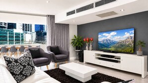 Ett modernt vardagsrum med en stor tv-skärm, två grå fåtöljer, en vit soffa och ett soffbord.
