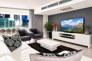 A modern living room with a large flat-screen TV, two grey armchairs, a white sofa, and a coffee table. - Table Mountain Signature Suite  City Views (Cape Town)