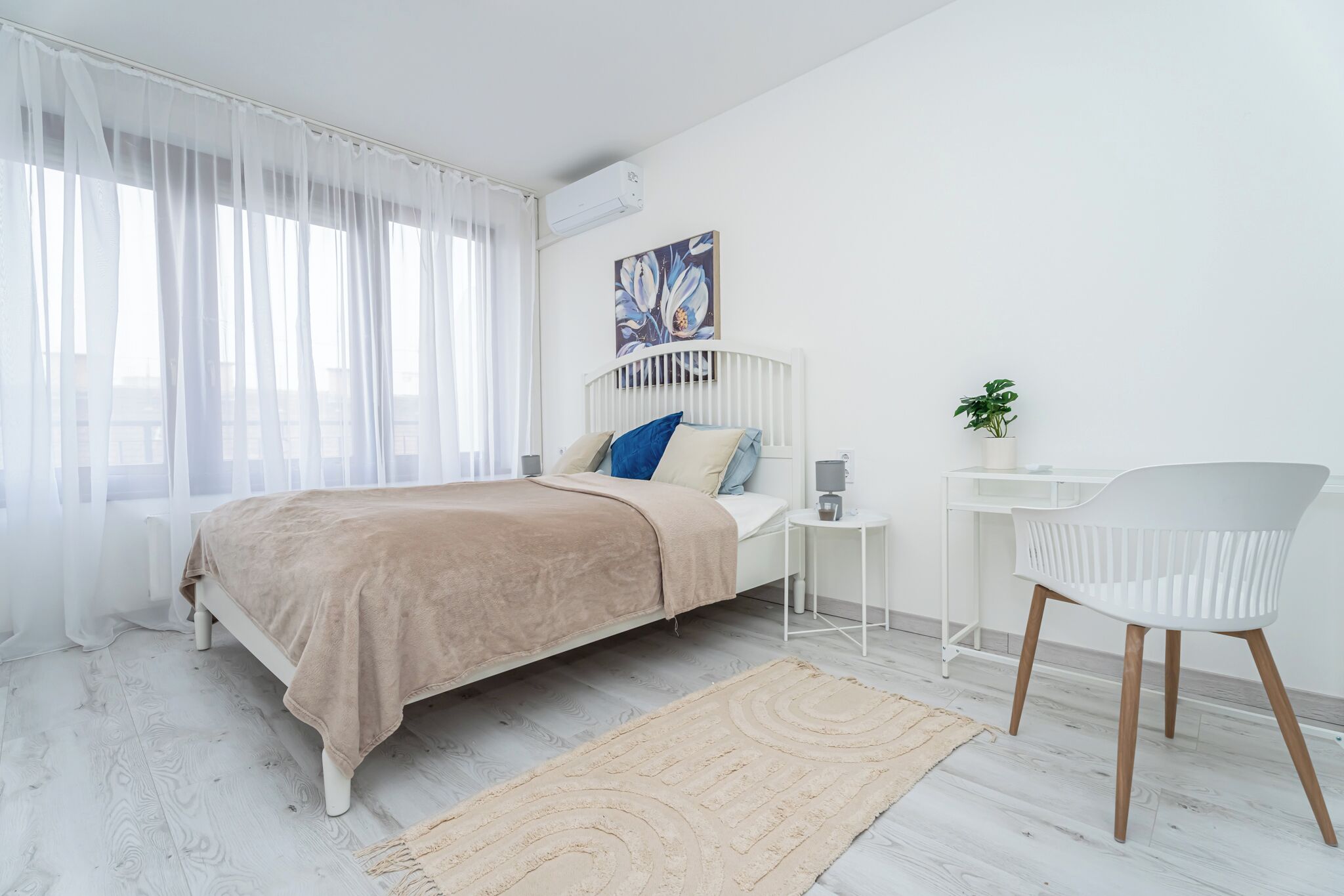 Une chambre à coucher comprenant un lit, une table de chevet, une chaise et un bureau agrémenté d’une plante.