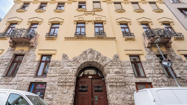Ein mehrstöckiges Gebäude mit einem steinernen Bogenportal, mehreren Balkonen und einer Reihe von Fenstern.