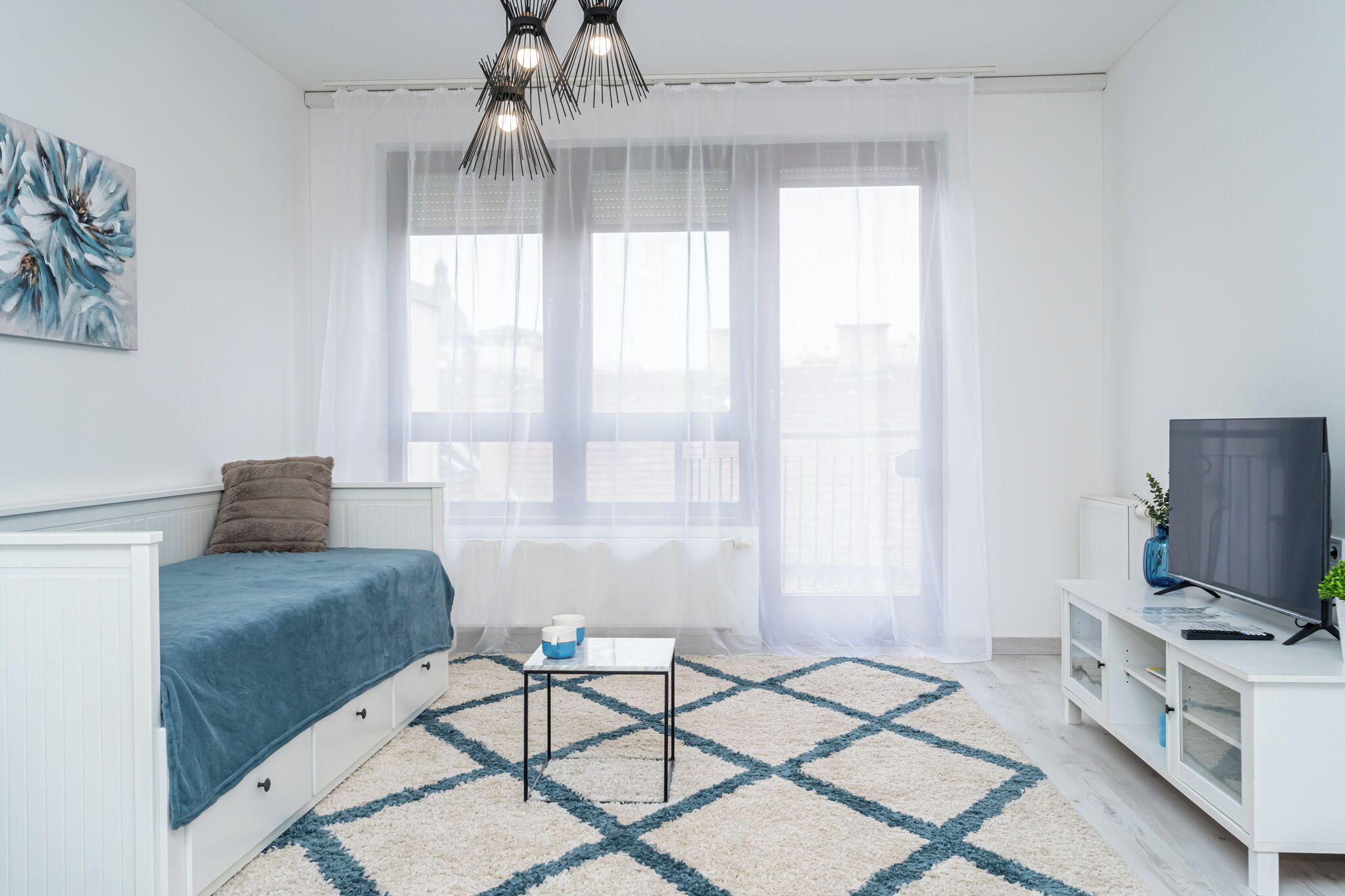Ein modernes Wohnzimmer mit einer Couch, einem Couchtisch, einem Fernseher und einem großen Fenster mit transparenten Vorhängen.