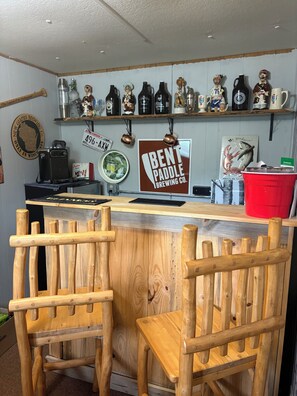 A bar with wooden chairs, a sign for Bent Paddle Brewing Co., and shelves with bottles and mugs. - Riverfront Cabin Retreat (Ojibwa)