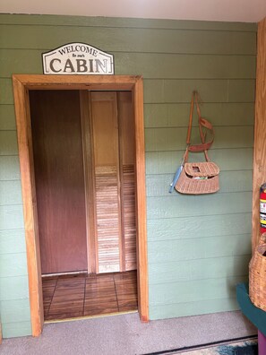 A wooden cabin entrance with a 'Welcome to our Cabin' sign, a wicker basket, and a fire extinguisher. - Riverfront Cabin Retreat (Ojibwa)
