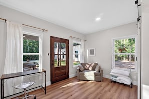 A room with a wooden floor, a sofa, a desk with a chair, and a window with curtains. - Stylish Farmstay on 6 Acres • Cowboy Pool • Fresh Eggs • Casita • Fire Pit (Tyler)