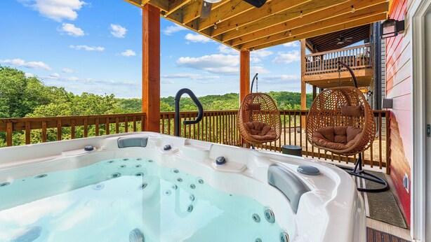 Un bain à remous sur une terrasse en bois, avec vue sur la verdure, un ventilateur de plafond et des fauteuils en osier.
