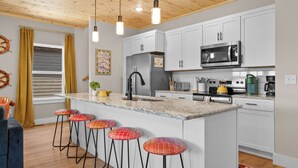 Une cuisine moderne avec des meubles blancs, un îlot central doté de tabourets, un four à micro-ondes et une cuisinière.