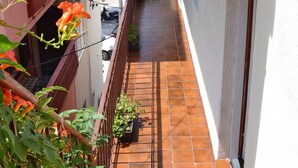 Un balcón estrecho con suelo de baldosas, baranda de metal y macetas con plantas.
