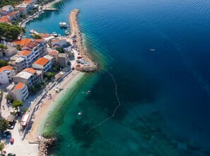 An aerial view of a coastal town with buildings along the waterfront, clear blue water, and a rocky shoreline. - Olive Grove Apartment (Podgora)