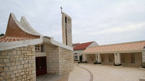 Un patio con una iglesia que presenta una torre con reloj, muros de piedra y un techo de tejas.