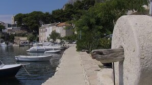Un muelle con barcos amarrados, un muro de piedra y edificios al fondo.
