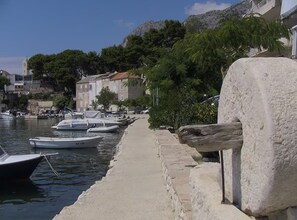 A waterfront with boats docked, a stone wall, and buildings in the background. - Olive Grove Apartment (Podgora)