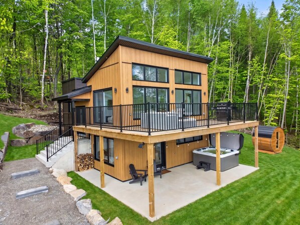 Eine moderne, zweigeschossige Holzhütte mit Balkon, Whirlpool und Terrasse.