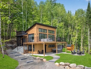 Eine zweistöckige Holzhütte mit Balkon, Whirlpool und Kamin in einer Waldlandschaft.