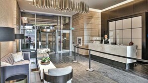 Un moderno vestíbulo de hotel con mostrador de recepción, área de descanso y una lámpara de techo única.