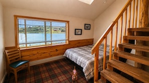 A bedroom with a large window, a bed, a wooden bench, and a staircase.