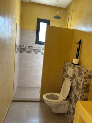 A bathroom with a shower, toilet, and a window.