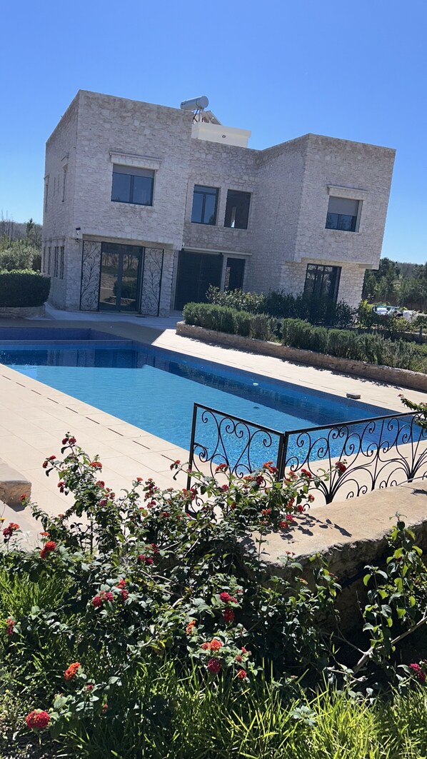 A two-story stone building with a swimming pool and a metal fence in the foreground.