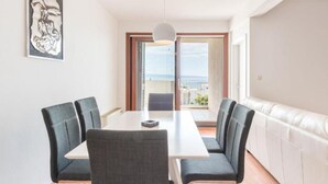 A dining area with a table and four chairs, a pendant light, a framed artwork on the wall, and a view of the sea through a sliding door. - Apartments Adriatic (Split)