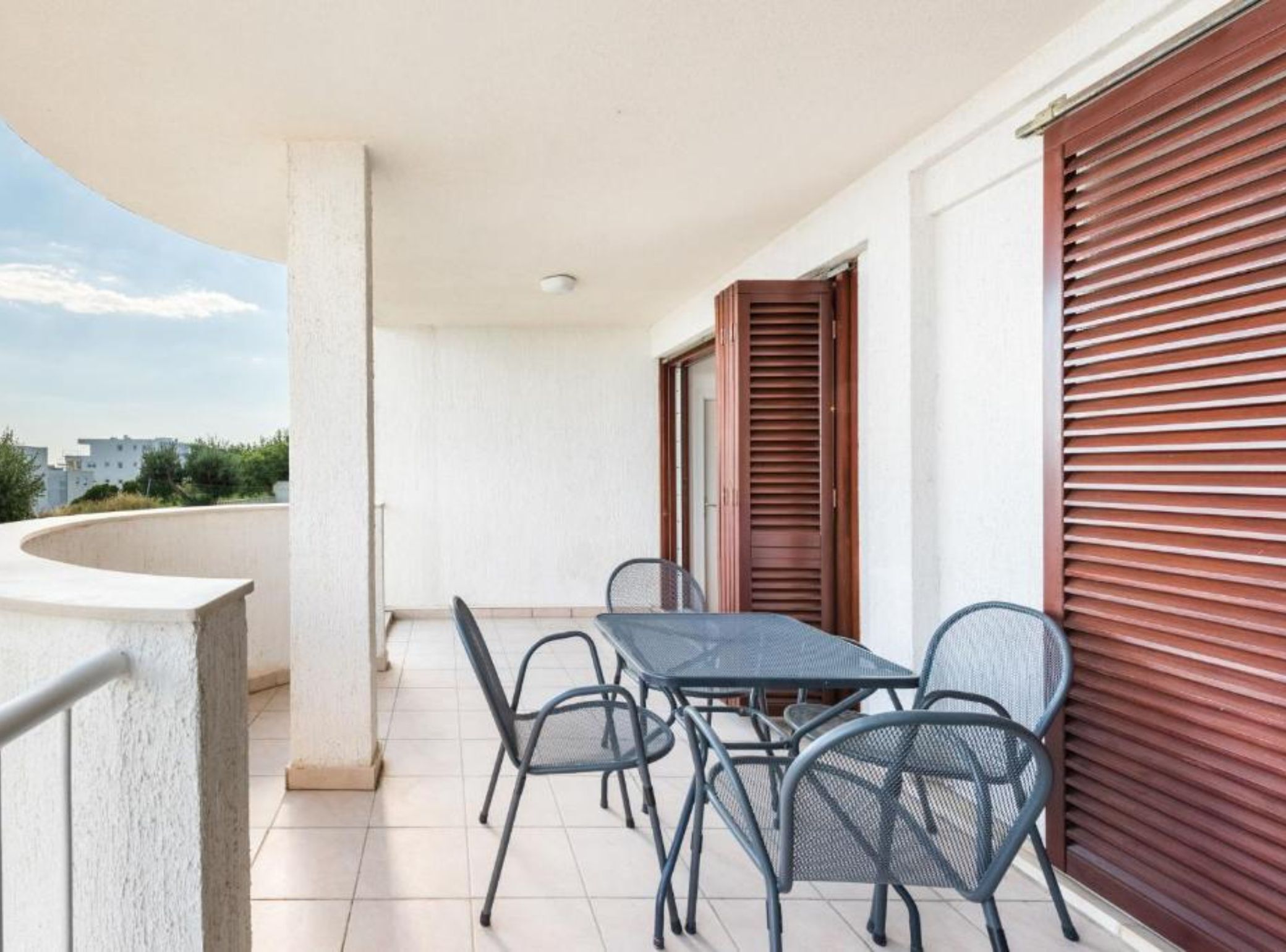 Un balcone con tavolo e sedie, vista sulla città e una persiana chiusa.