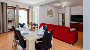 A dining area with a wooden table set for four, a red sofa, and a kitchen area with cabinets and a TV. - Apartments Adriatic (Split)