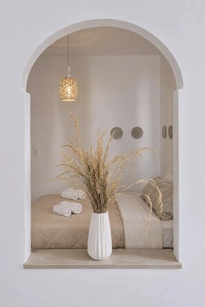 Una habitación minimalista con una cama, una lámpara colgante y un jarrón blanco con plantas secas.