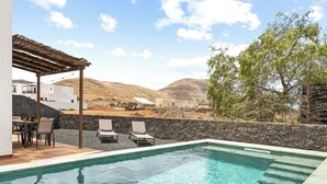 Ein Pool mit Liegestühlen, einer Pergola und Blick auf eine Hügelkette.