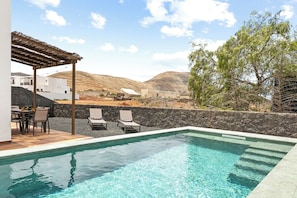 Ein Pool mit Liegestühlen, einer Pergola und Blick auf eine Hügelkette.