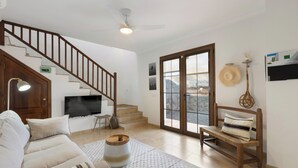 Ein Wohnzimmer mit Sofa, einer Holzbank, einem Fernseher, einem Deckenventilator und einer Treppe.