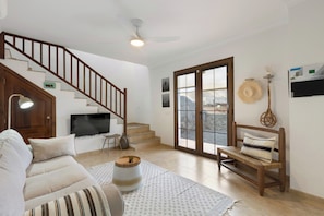 Ein Wohnzimmer mit Sofa, einer Holzbank, einem Fernseher, einem Deckenventilator und einer Treppe.