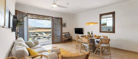 A spacious living area with a sofa, dining table, chairs, a TV, and a view of the outdoors.