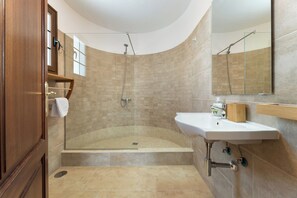 Un baño moderno con ducha envuelta en vidrio, lavamanos blanco y tocador de madera.