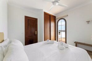 A hotel room with a bed, a ceiling fan, a wooden door, and a window with a view. - Home2Book Exclusive Villa Volcán Art & Light (Yaiza)